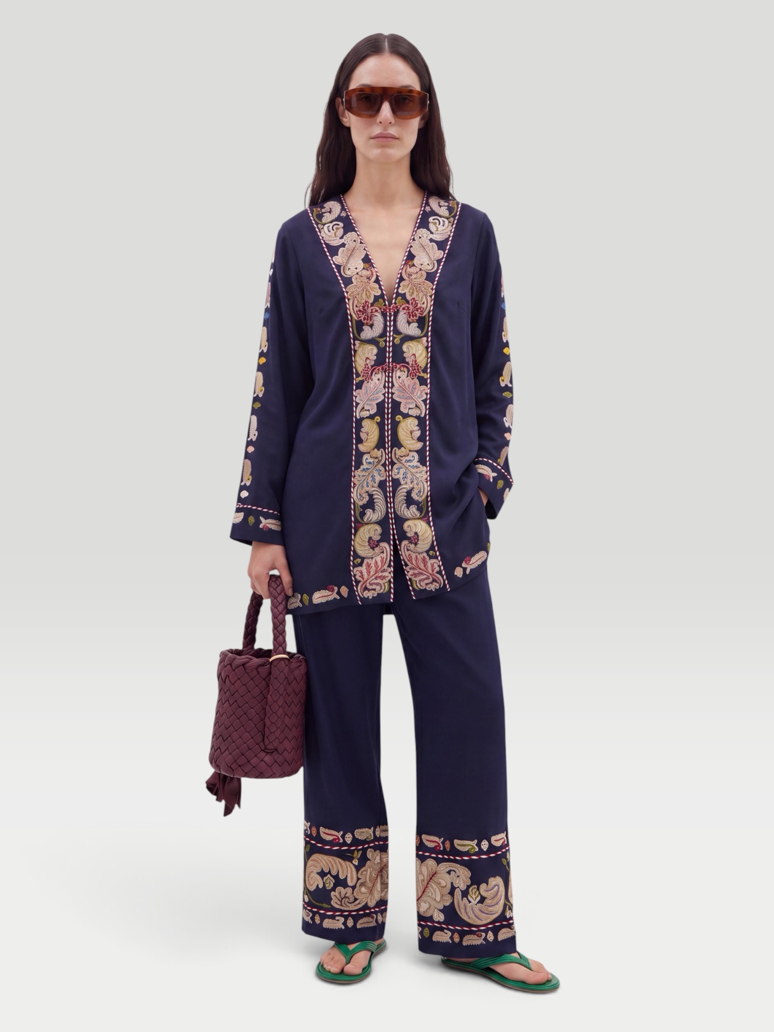 BODE Feather Runner Embroidered Cotton-Blend Flared Pants in black, worn with BODE Feather Runner Embroidered Cotton-Blend Twill Jacket, Dries Van Noten Oval Sunglasses, Bottega Veneta Kalimero Città Small Leather Shoulder Bag, Bottega Veneta Sampieri Flat Thong, on the water. Styled by Sharon Lombardo for FDV Concierge.