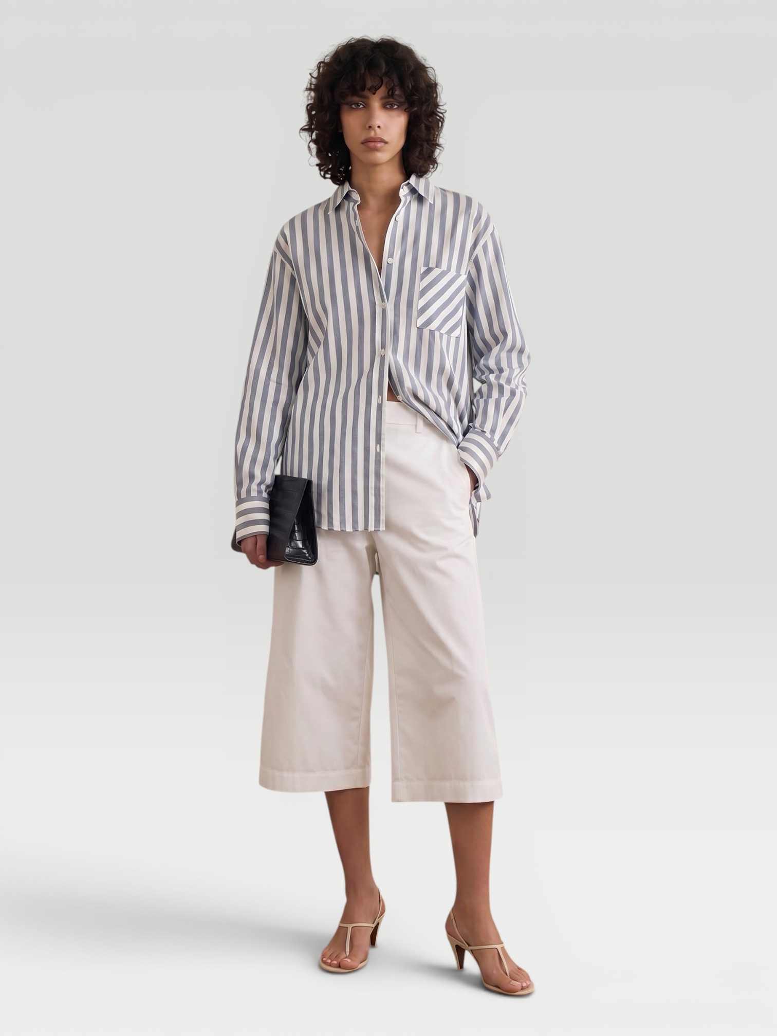 Jacquemus Le Marin High Rise Shorts in white, worn with Jacquemus Striped Shirt, Bottega Veneta Small Onda Clutch, Neous Arneb 65 Sandals. Styled by Sharon Lombardo for FDV Concierge.