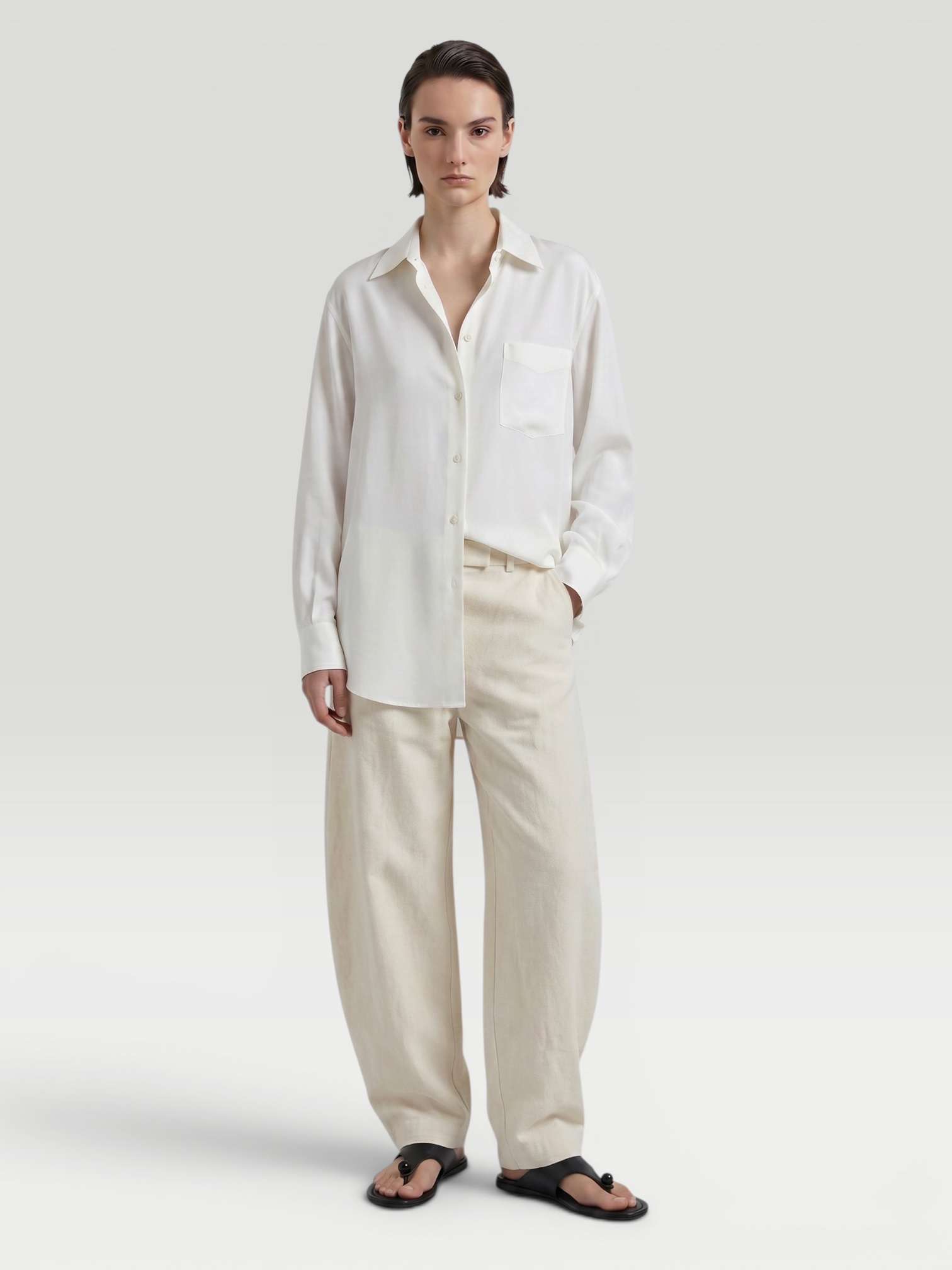 Loro Piana Andre Linen Shirt in white, worn with Coperni One-Shoulder Logo-Plaque Swimsuit, Bottega Veneta Sampieri Flat Thong, Arhaus Rivi Beach Towel, Loewe Leather-Trimmed Raffia Tote, on the water. Styled by Sharon Lombardo for FDV Concierge.