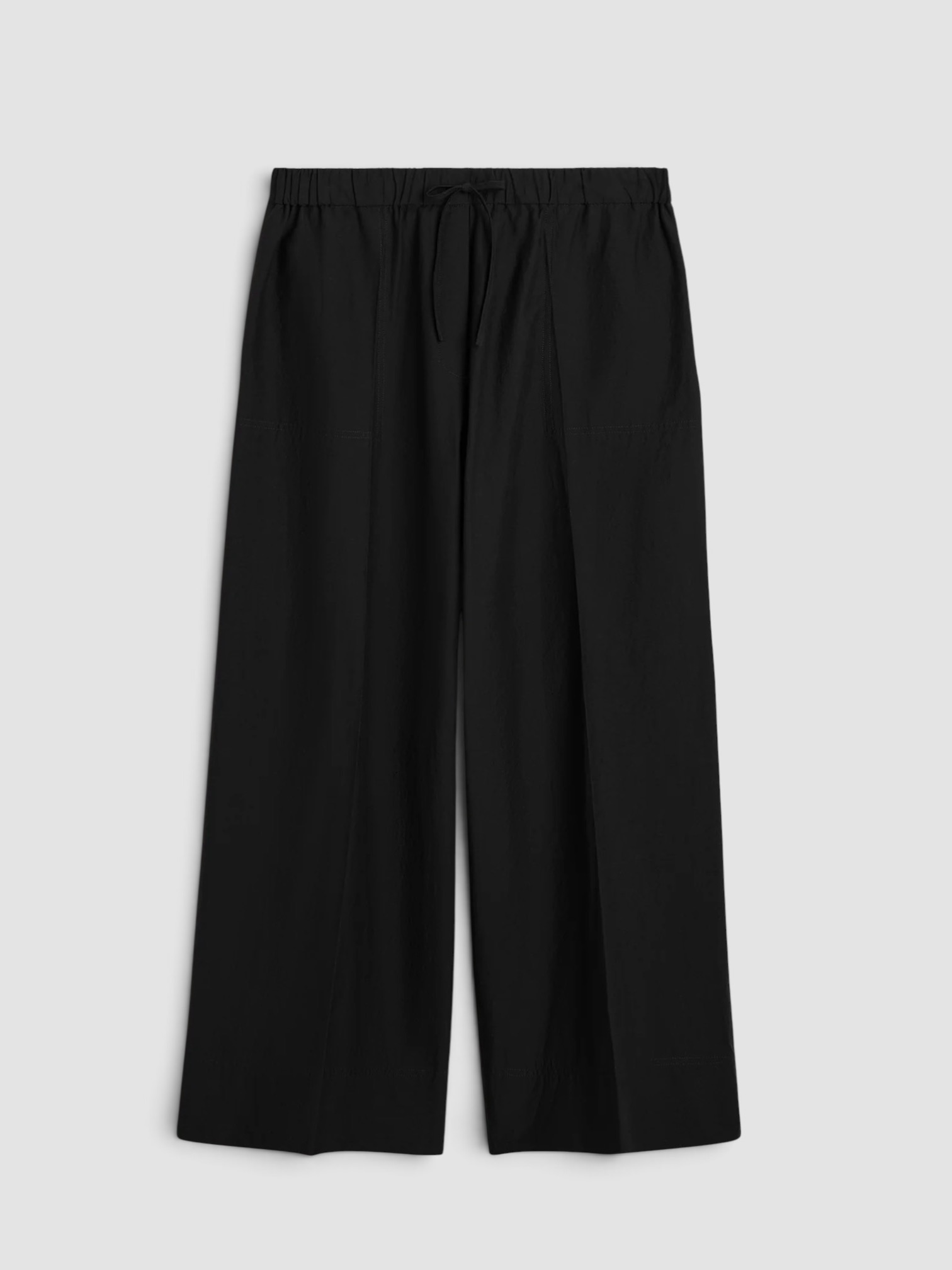 Totême Wide Summer Trousers in black, worn with All Three Kristen Rib Tank, St. Agni Fringed Leather Belt Skirt, Bottega Veneta Sampieri Flat Thong, Loewe Paula's Ibiza Punch Hole Small Leather-Trimmed Raffia Tote, on the water. Styled by Sharon Lombardo for FDV Concierge.